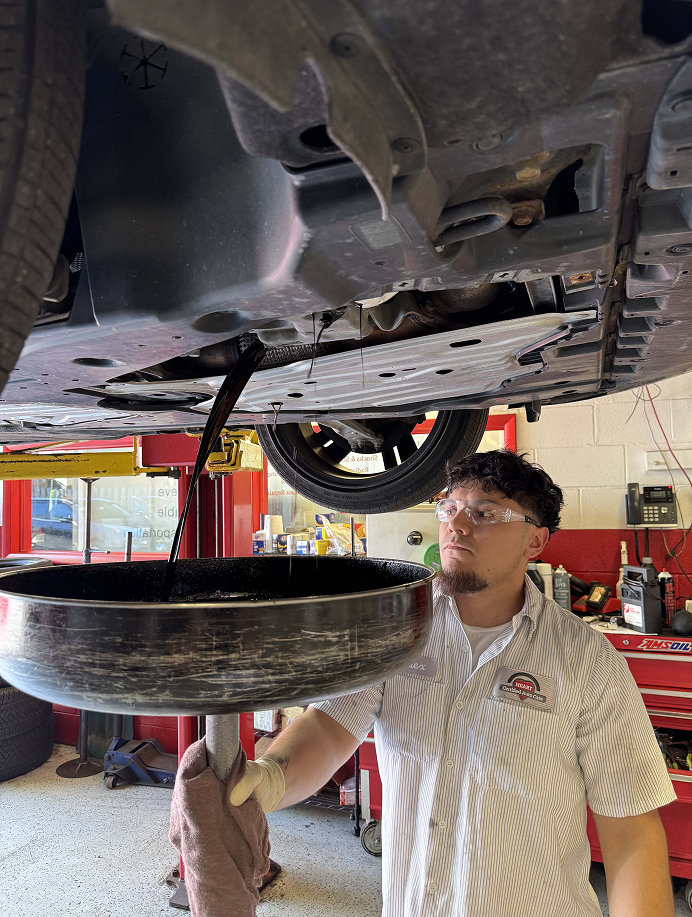 Technician performing an oil change inspection under a raised vehicle at HEART Certified Auto Care